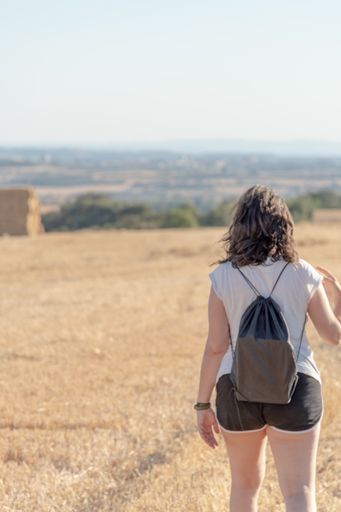 A vertical shot of a young Caucasian woman walking in a big open field on a hot summer day