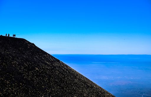 A silhouette of people standing on top of a hill near the sea with clear blue sky in the background