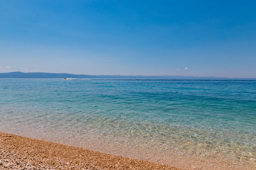 A closeup shot of a beach with beautiful blue waves and a hill in the background