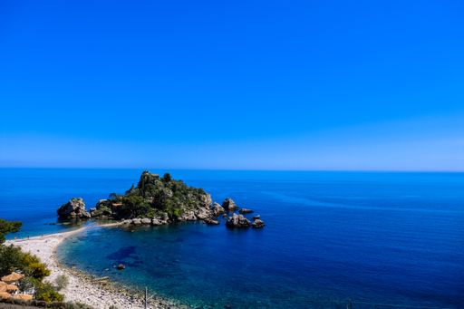 An aerial shot of mossy rocks near the sea with clear blue sky in the background