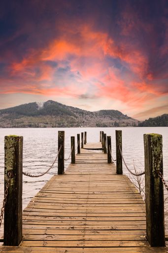 A vertical shot of a wooden dock with fences on the sea under a cloudy sky during a beautiful sunset
