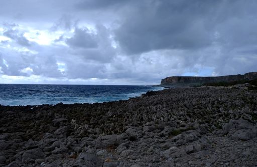 A rocky shore near the sea with a mountain in the distance under a cloudy sky