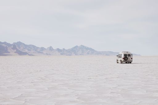 A solitary van on the vast Bonneville Salt Flats with distant mountains under a clear sky.