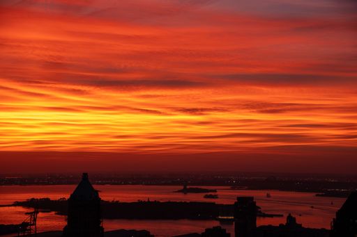 Vibrant sunset over New York City skyline with silhouetted buildings and glowing orange sky.