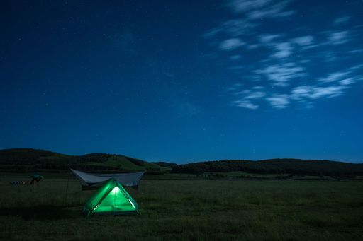 A serene night camping scene with a glowing tent under a starry sky