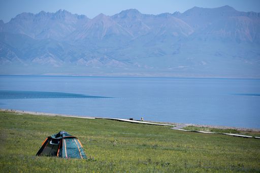 A serene lakeside camping scene with a tent on green grass, mountains in the background