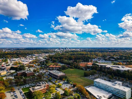 Aerial view of Raleigh, North Carolina, showcasing urban landscape and lush greenery under a vibrant blue sky with fluffy clouds.