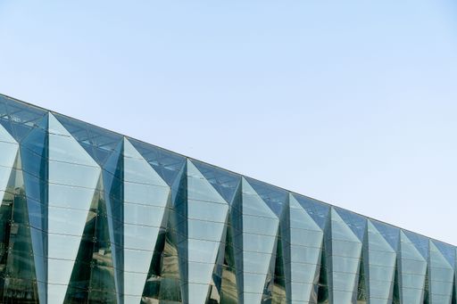 Modern glass architecture with geometric patterns against a clear blue sky.