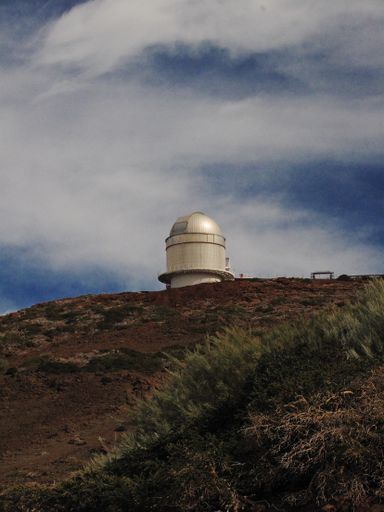 A vertical shot of an observatory on a hill with cloudy sky in the background