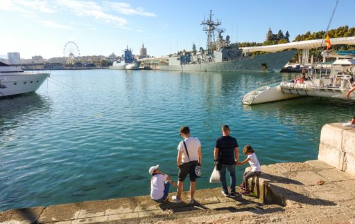 A family at Muelle Uno quay in Port of Malaga, with two warships in background, Andalusia, Spain