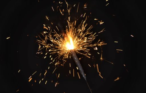 A close-up of a sparkler igniting with bright sparks against a dark background