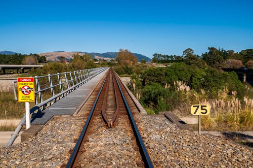 Railway tracks stretching into the distance with a warning sign and lush greenery under a clear blue sky.