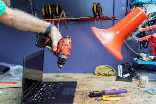 A male hand holding a cordless drill while repairing the broken lapto
