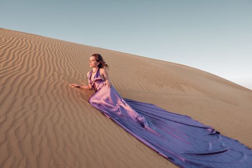 A gorgeous Caucasian woman wearing an purple long dress and posing for the camera in a desert