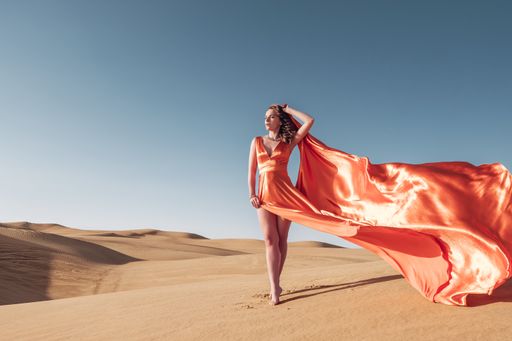 A gorgeous Caucasian woman wearing an orange long dress and posing for the camera in a desert