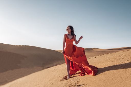 A gorgeous Caucasian woman wearing an orange long dress and posing for the camera in a desert