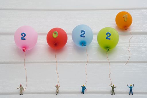 Bunte Luftballons mit einer Zahl von Miniatur Menschen gehalten ergeben  2022 . Die Zahl eins fliegt davon. Konzept: Jahreswechsel 2021 zu 2022