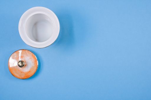 A top view of an orange empty cup next to a cover on a blue isolated background with free space