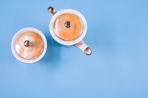 A top view of an orange covered teapot, a covered cup on a blue isolated background with free space