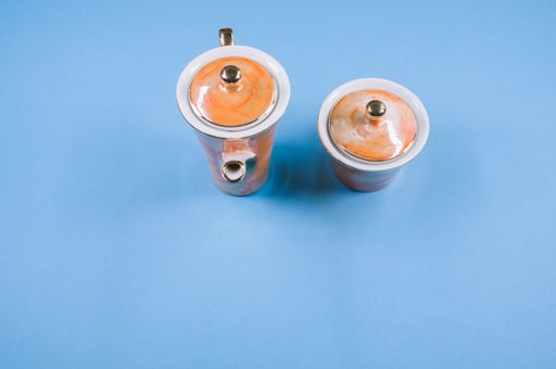 A top view of an orange covered teapot, a covered cup on a blue isolated background with free space