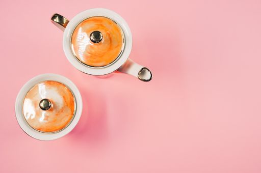 A top view of an orange covered teapot, a covered cup on a pink isolated background with free space