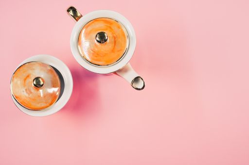 A top view of an orange covered teapot, a covered cup on a pink isolated background with free space