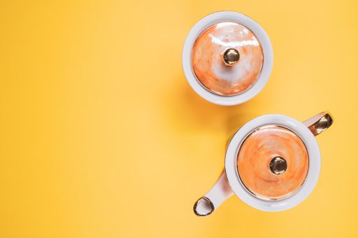 A top view of an orange covered teapot, a covered cup on an orange isolated background with free space