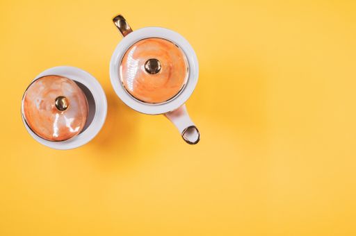 A top view of an orange covered teapot, a covered cup on an orange isolated background with free space