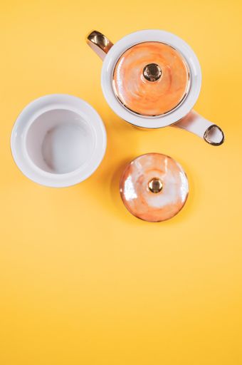 A top view of an orange covered teapot, cup and a cover on an orange isolated background with free space