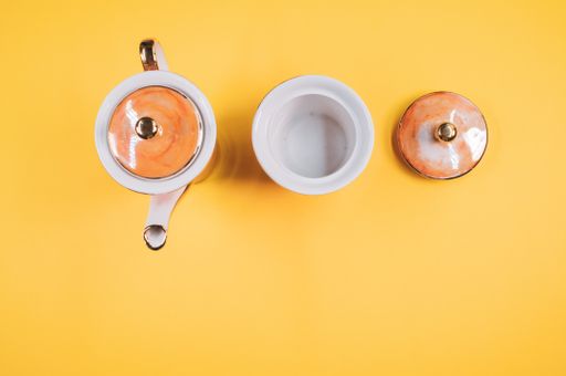 A top view of an orange covered teapot, cup and a cover on an orange isolated background with free space