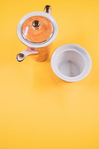 A top view of an orange ceramic cup next to a n empty cup on a yellow isolated background with free space