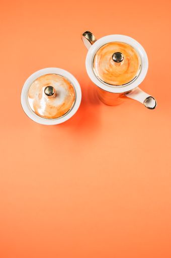 A top view of an orange covered teapot, a covered cup on an orange isolated background with free space