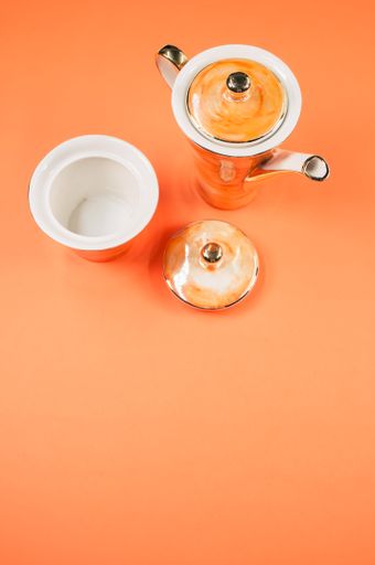 A top view of an orange covered teapot, cup and a cover on an orange isolated background with free space