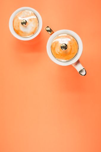 A top view of an orange covered teapot, a covered cup on an orange isolated background with free space