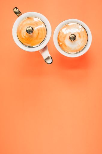 A top view of an orange covered teapot and a covered cup on an orange isolated background, free space