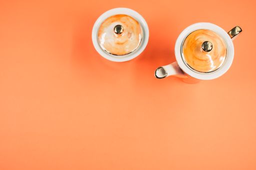 A top view of an orange covered teapot, a covered cup on an orange isolated background with free space