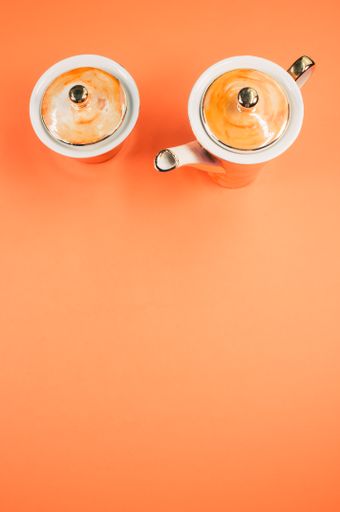 A top view of an orange covered teapot, cup and a cover on a blue isolated background with free space