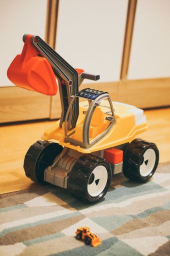 A vertical shot of a plastic toy excavator on a carpeted floor