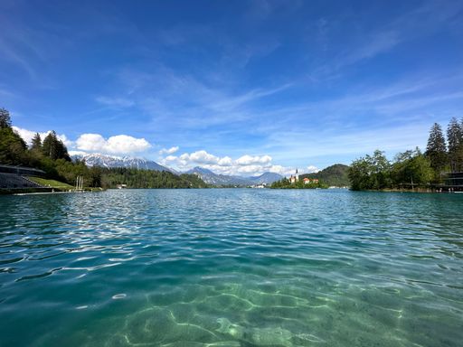 Scenic view of Lake Bled with clear turquoise water and mountains in the background under a bright blue sky in Slovenia.