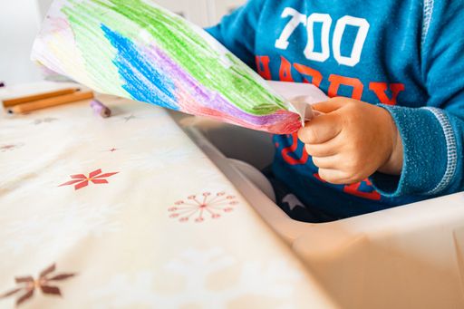 A child drawing on the paper with colorful pencils