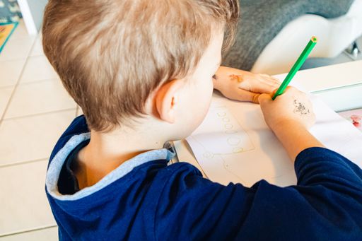 A child drawing on the paper with colorful pencils