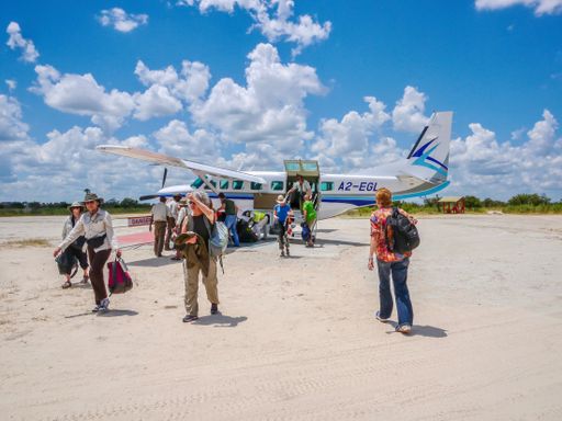 A small group of American safari guests disembark a light aircraft on a rural landing strip in Africa.