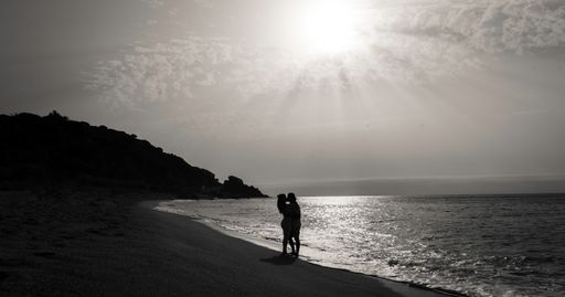 A grayscale shot of a couple kissing on a scenic beach