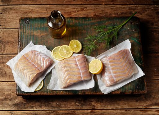A top view of fresh raw pollack fish fillet slices on a wooden board with herbs and spices