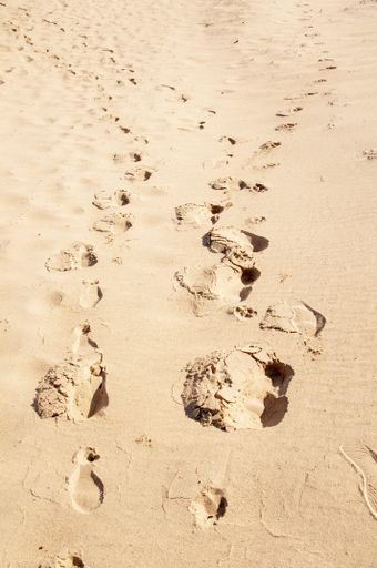A vertical shot of a sandy beach with feet trails on the sand during a sunny day