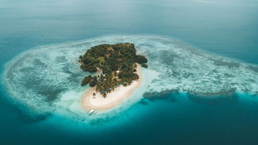 Aerial view of a tropical island surrounded by turquoise waters and coral reefs, featuring lush greenery and a sandy beach.