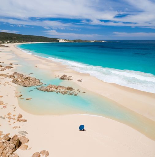 Aerial view of a pristine beach with turquoise waters, white sand, and a lone blue umbrella, capturing a serene coastal landscape.