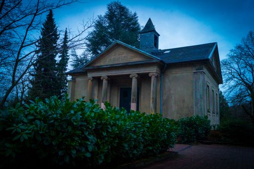 A building constructed like a Roman temple under a clear blue evening sky with dark bushes around it