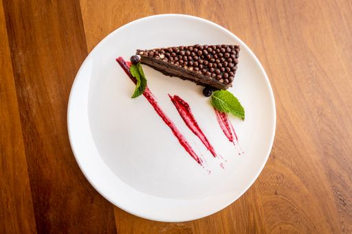 A top view of a slice of a chocolate cake on a plate with mint leaves and syrup for decoration