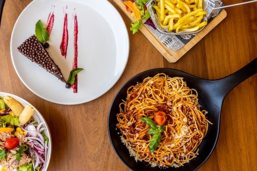 A top view of a table in a cafe full of food including plates of pasta, salads, and a slice of cake
